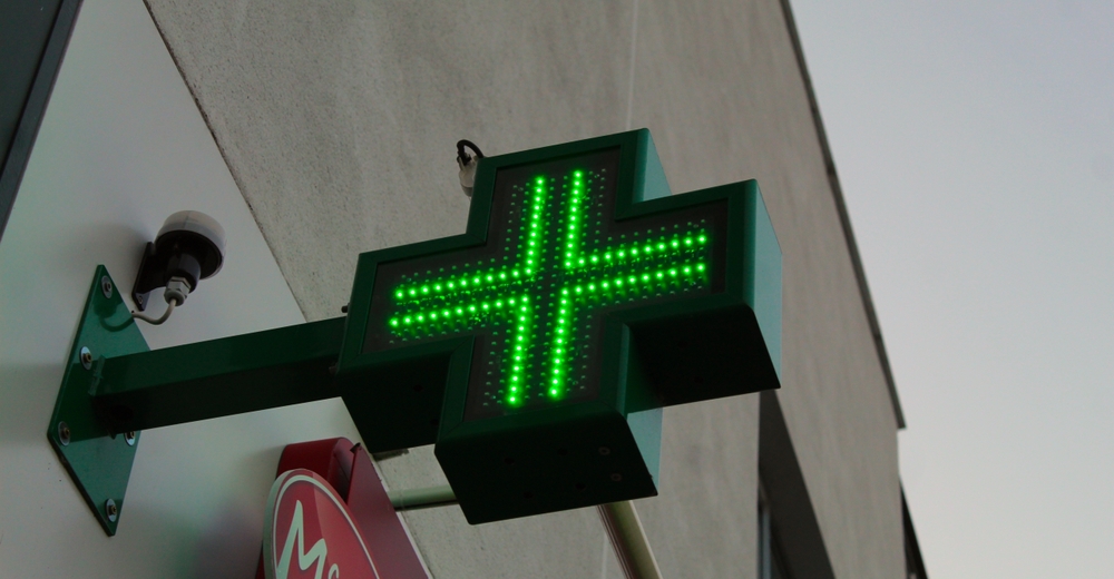 Apteczny zielony neonowy krzyż na elewacji apteki.