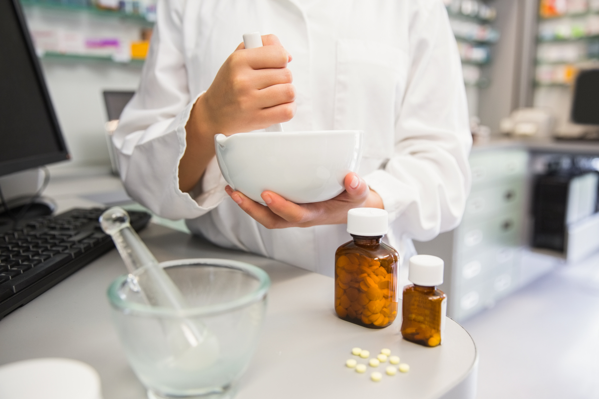 Farmaceutka uciera w moździerzu lek, na biurku butelki z lekami i komputer.