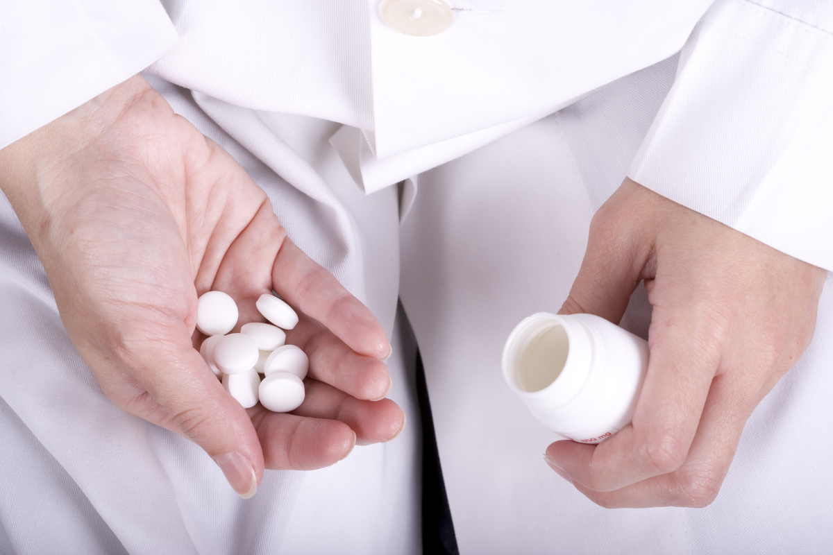 Farmaceuta trzymający w dłoni wiele tabletek, w drugiej dłoni słoiczek po leku.