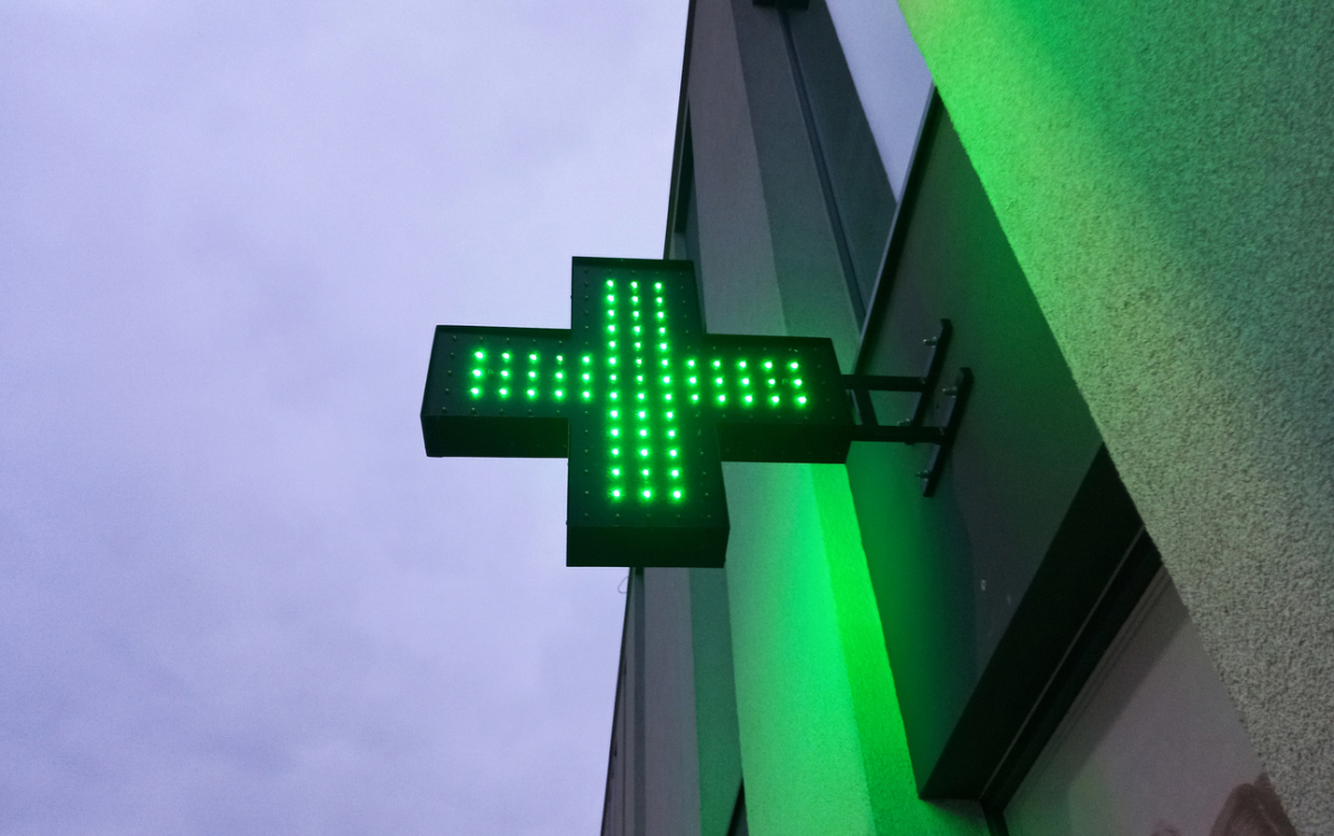 Apteczny krzyż na elewacji budynku i ciemne niebo nocą