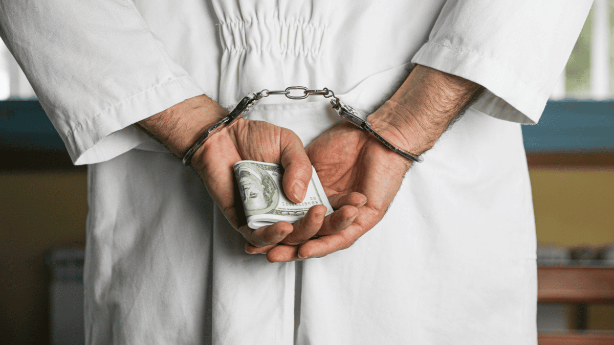 Człowiek w fartuchu zakuty kajdankami trzyma banknoty w dłoniach (fot. istockphoto.com)