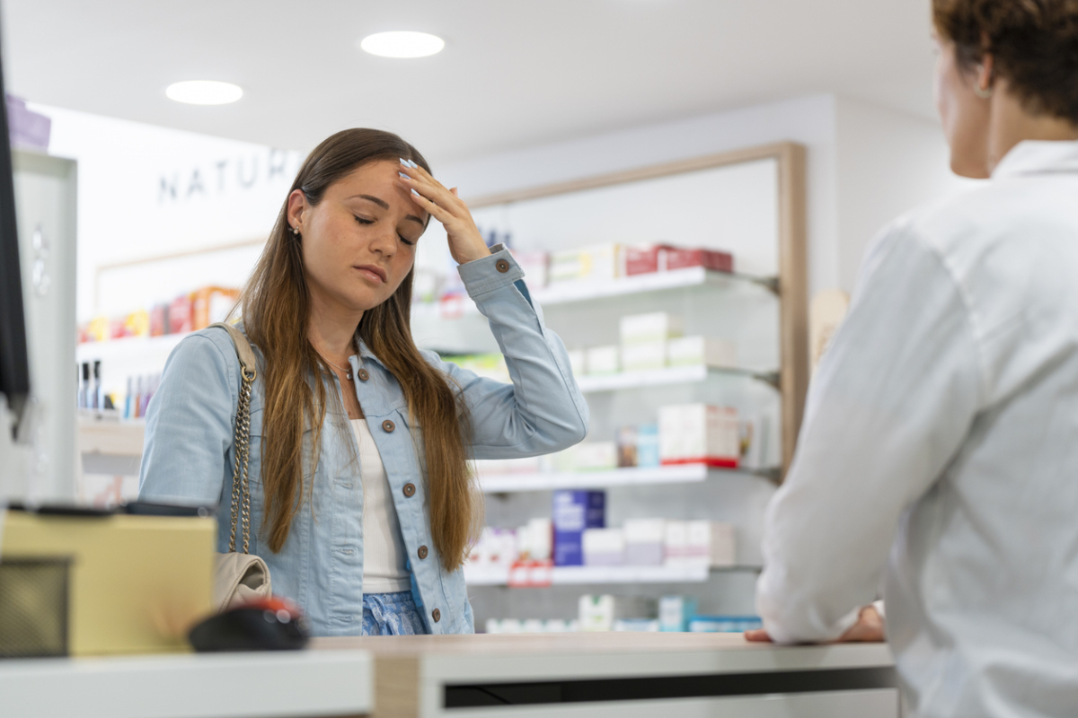 Nastolatka w aptece rozmawia z farmaceutą i trzyma się za głowę