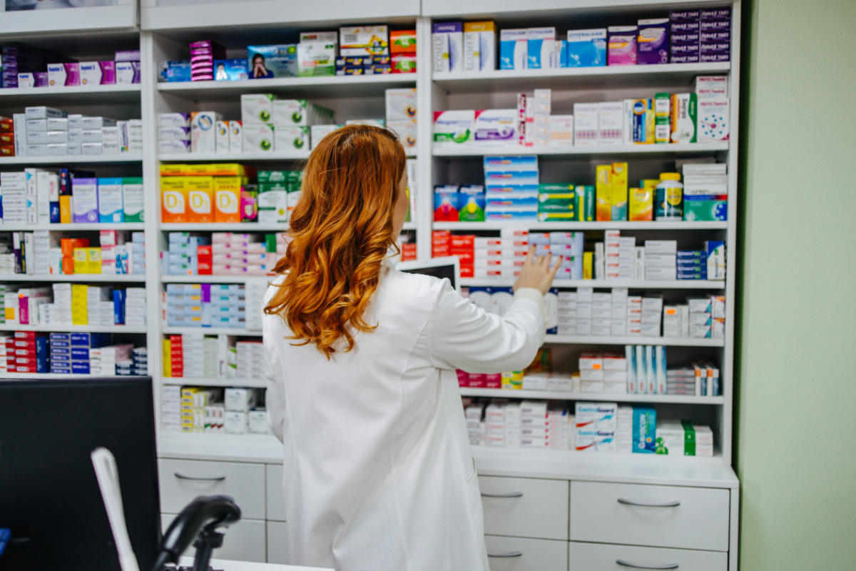 Farmaceutka w aptece układa opakowania leków na półkach