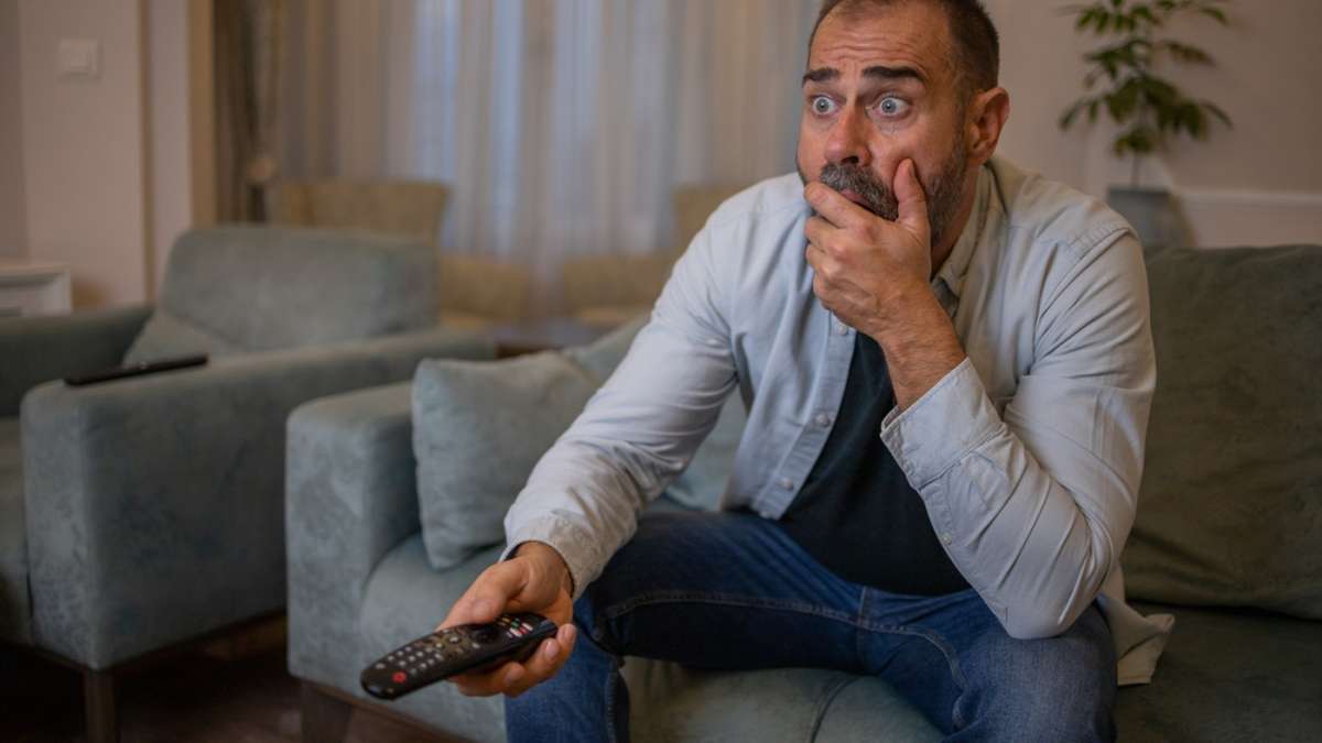 starszy mężczyzna zakrywa usta oglądając telewizję