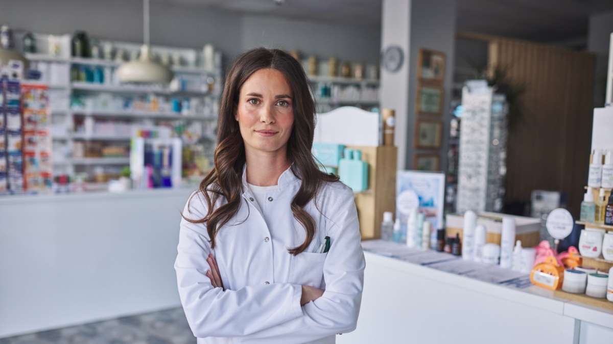 Farmaceutka stoi w aptece z założonymi rękami